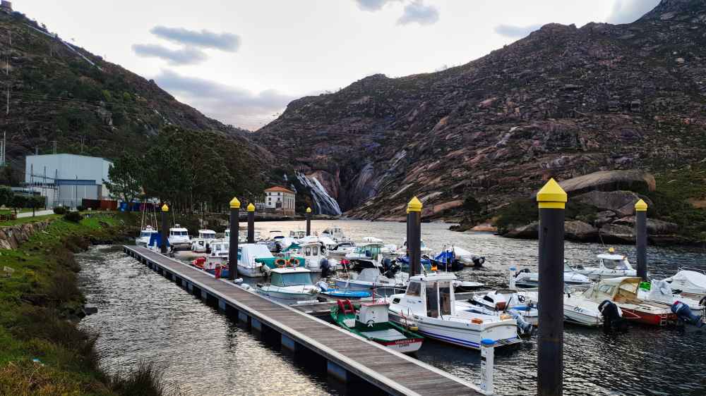 Barcos en el puerto deportivo de Ézaro con la central eléctrica y la cascada de fondo
