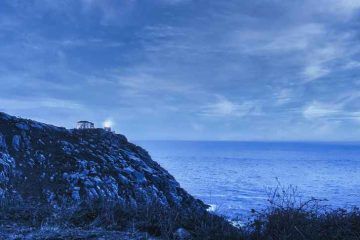 Faro de Finisterre encendido sobre el acantilado del ocรฉano Atlรกntico durante el viaje a Galicia en furgoneta camper de Van and to Discover