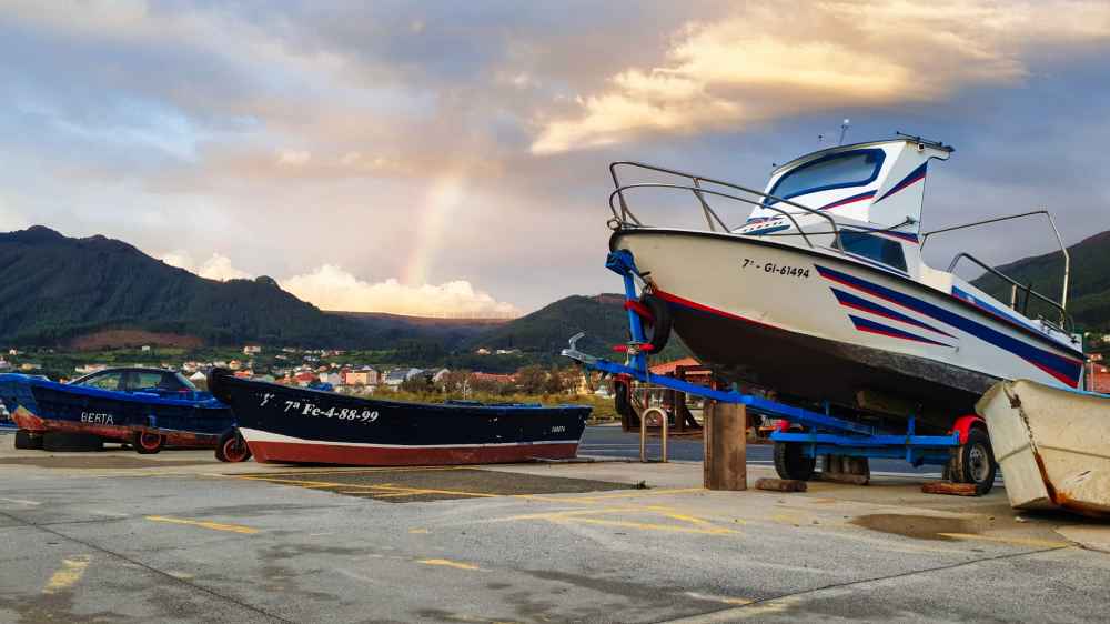 Barcos tradicionales en el puerto de Cariรฑo con las montaรฑas y el arcoรญris de fondo Foto realizada por Juanma y Elena de Van and to Discover en la ruta por Galicia en furgoneta camper