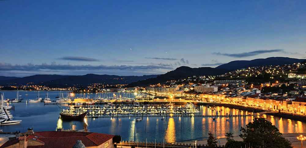 Foto nocturna del puerto deportivo de Bayona con las luces y los barcos reflejándose en el agua.
