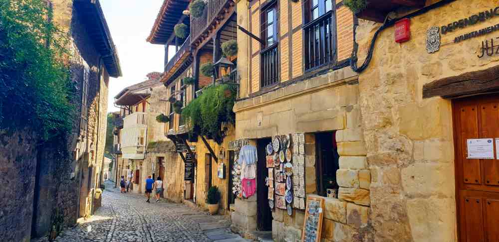 Calles medievales empedradas con balcones de madera y tiendas de recuerdos en Santillana del Mar - Van and to Discover