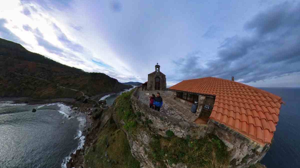Juanma y Elena de Van and to Discover frente a la ermita de San Juan de Gaztelugatxe contemplado los acantilados en su ruta en furgoneta camper por Paรญs Vasco